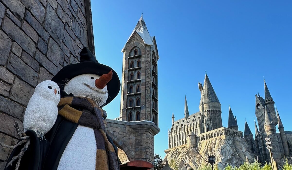 Hogsmeade Snowman wearing a Hufflepuff scarf with Hogwarts castle in distance in The Wizarding World of Harry Potter at Universal Orlando