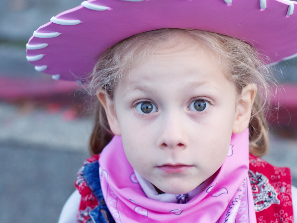 little girl in pink cowgirl hat making a surprised face